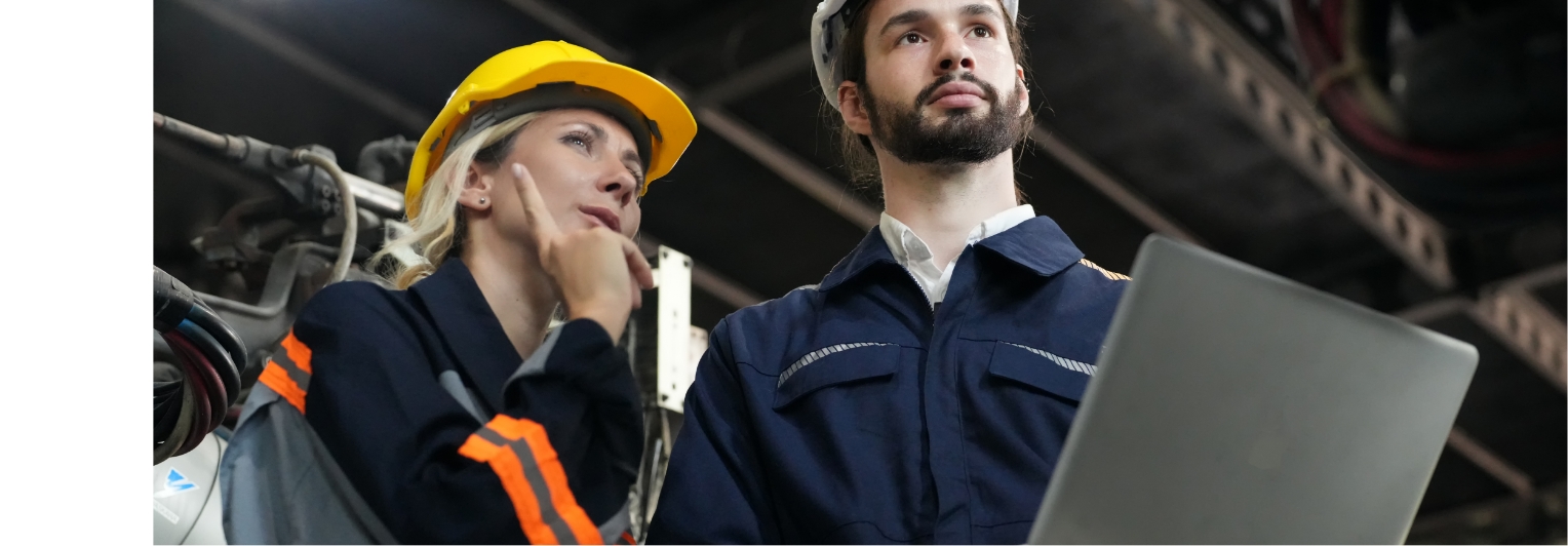 A man and woman in hard hats are looking at a laptop.