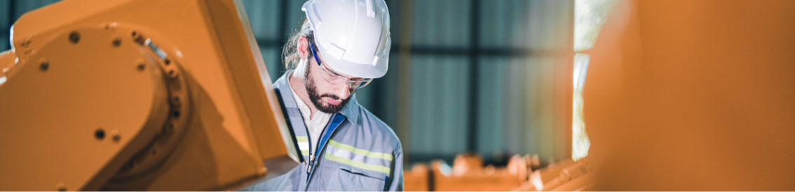 A man in a hard hat is looking at a machine.