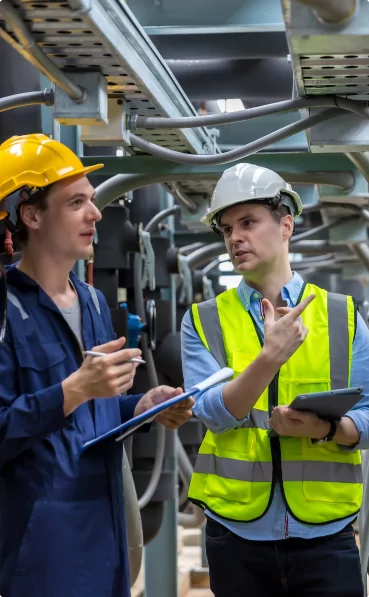 Two men in hard hats talking to each other in a factory.